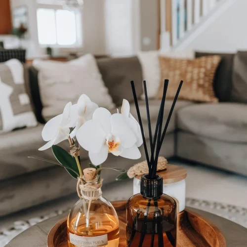 reed-diffuser-with-black-sticks-yellow-liquid-table-front-view-white-orchid-flower-nearby-gray-sofa-it-light-background